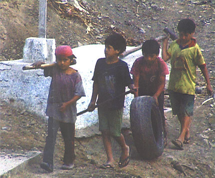 Peruvian children carry their sledgehammers and a tire to burn to the rock quarry where they work. in The Back of the World